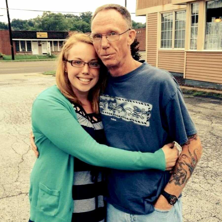 daughter poses with her father, she has her arms wrapped around him, he has his arm wrapped around her back