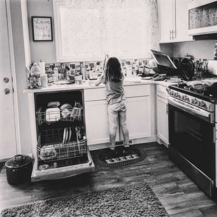 daughter stands in front of kitchen sink and helps to load the dishwasher