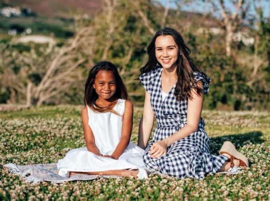 Young mom and daughter in dresses sitting on picnic blanket
