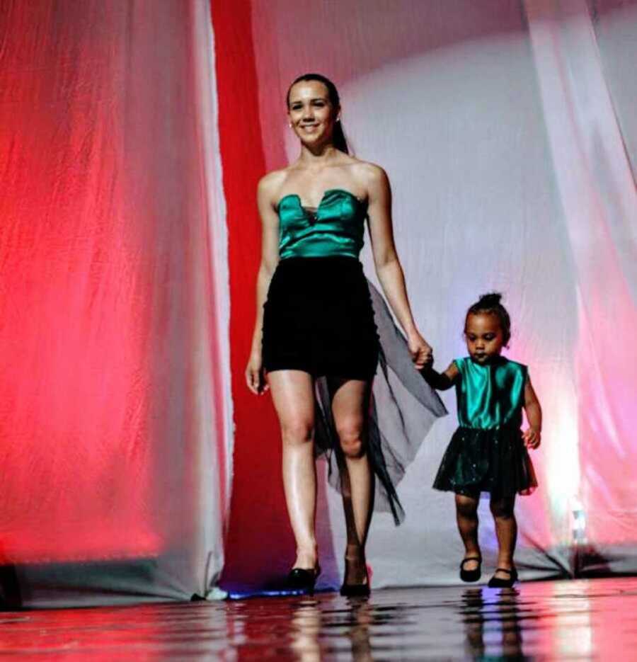 Teen mom walking down modeling runway with infant