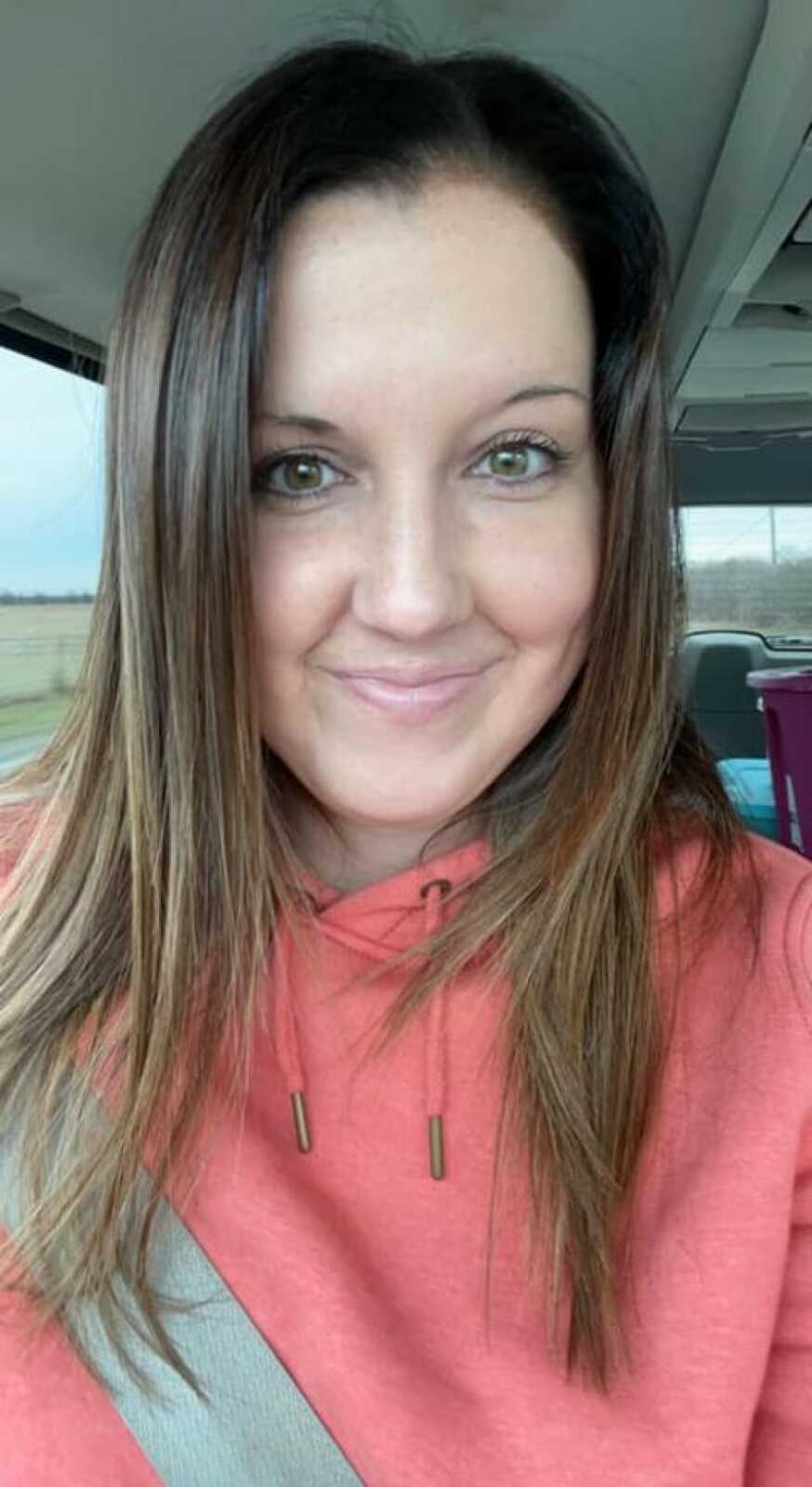 woman in a peach sweatshirt taking a selfie