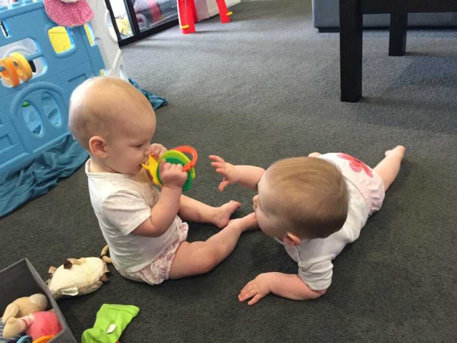 twin babies playing together while mom watches