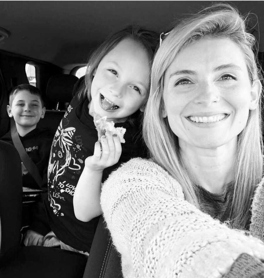 Mom of two smiles big for a car selfie with her children
