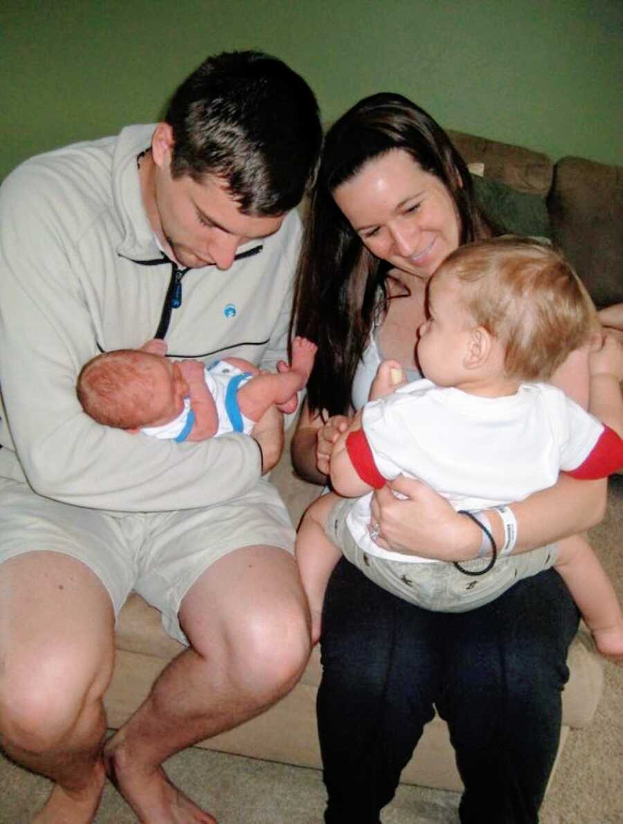 Young couple hold their toddler son and newborn as they meet for the first time