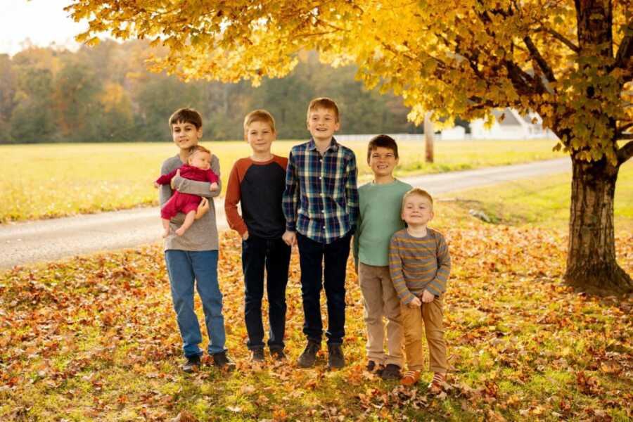 Fall-themed photo of five brothers holding their newborn baby sister