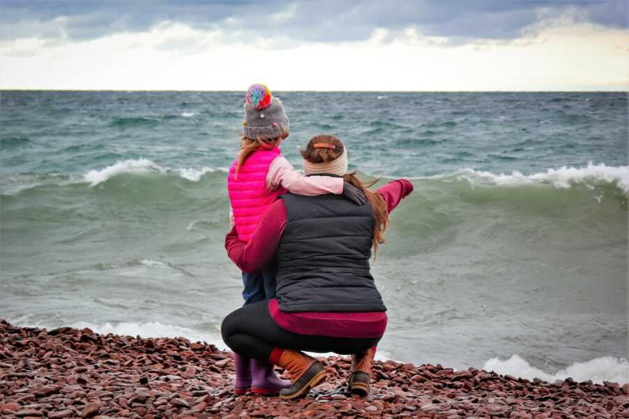 mother and daughter at a lake in Minnesota pointing at the water and wearing winter clothing
