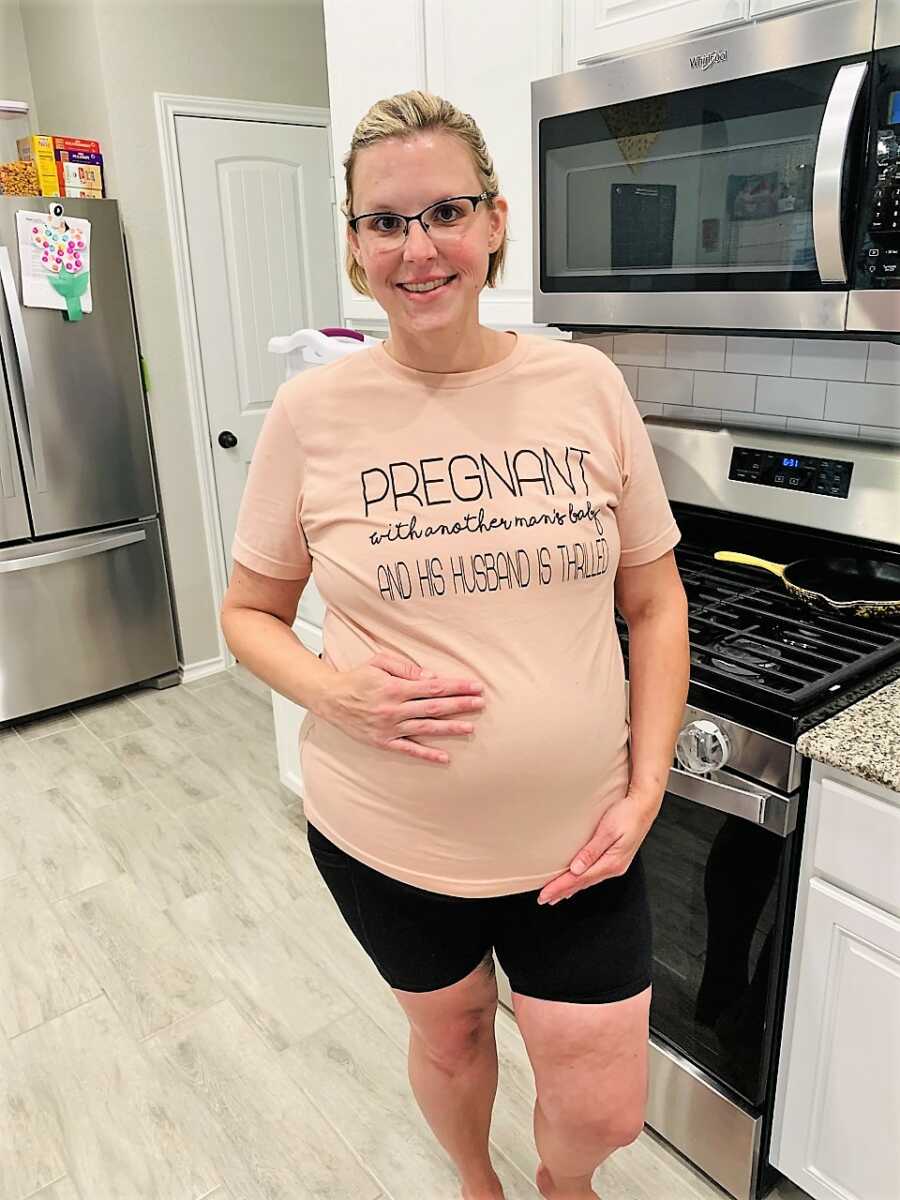 pregnant surrogate mom wearing a shirt that says pregnant with another man's baby and husband is thrilled
