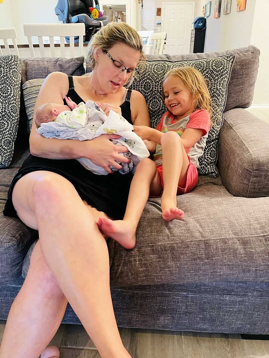 Postpartum mom holding newborn baby sitting next to daughter