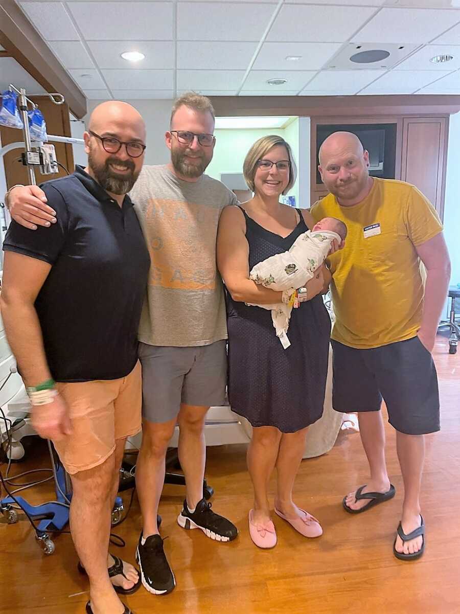 surrogate mother holding baby next to husband and gay parents 