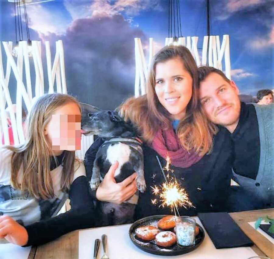 Blended family at a restaurant eating dessert while dog kisses girl's face
