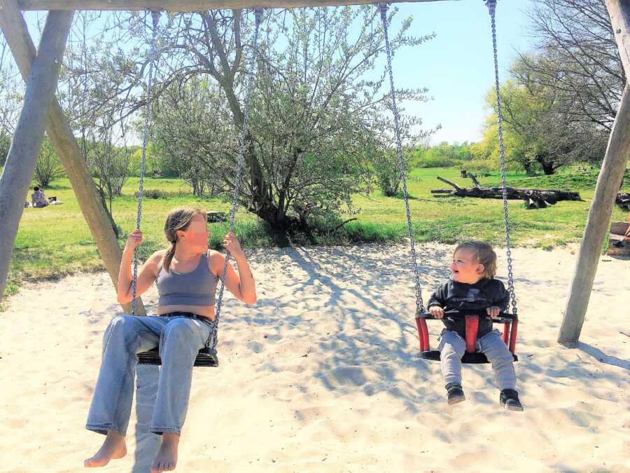 preteen sister and toddler brother playing in the swing at playground 