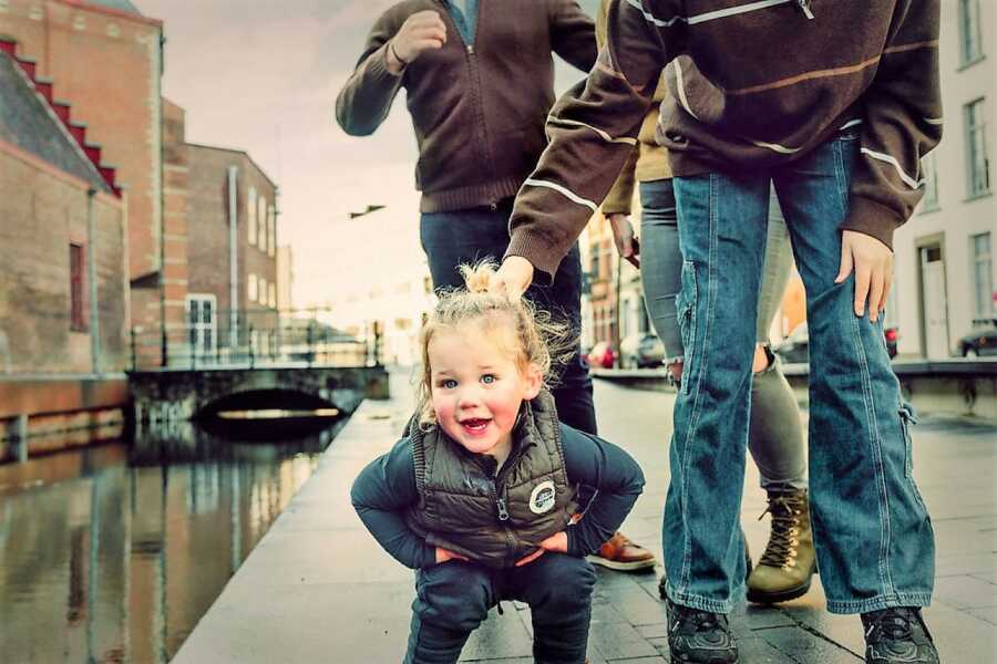 baby body squatting while looking at camera next to a water canal 