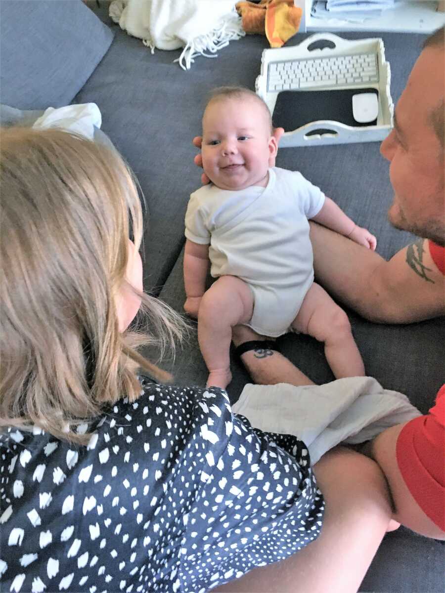 dad and sister stare at baby boy while laying in the couch 