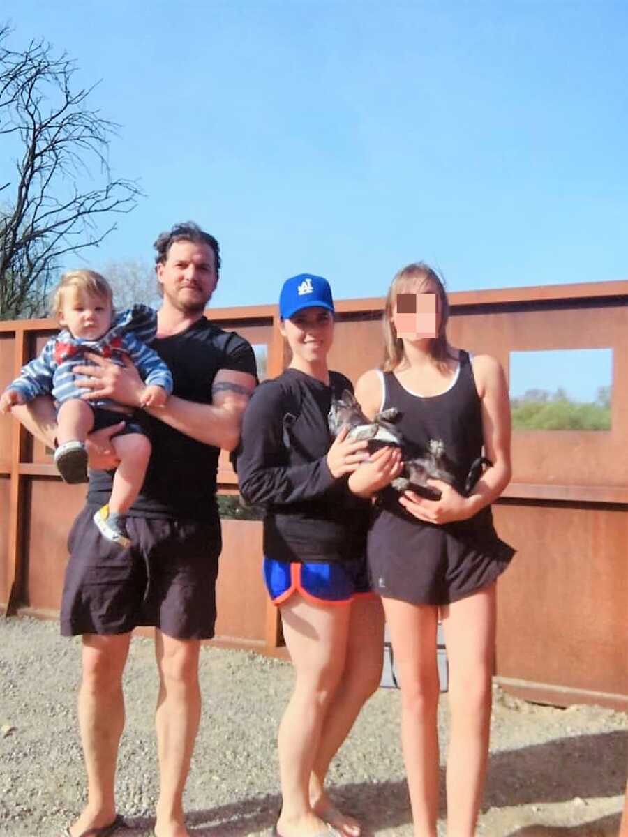 blended family wearing sports outfits holding baby and dog in arms 