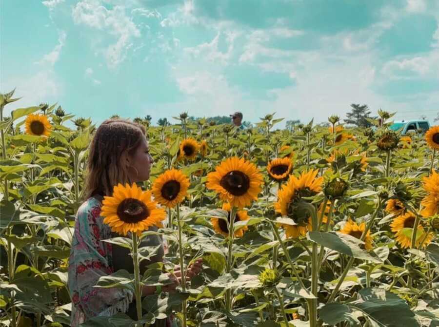 woman standing in the sunflowers being happy