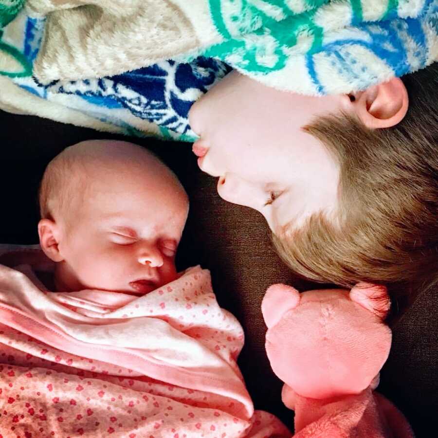 Little boy goes in for a forehead kiss on his sleeping newborn sister