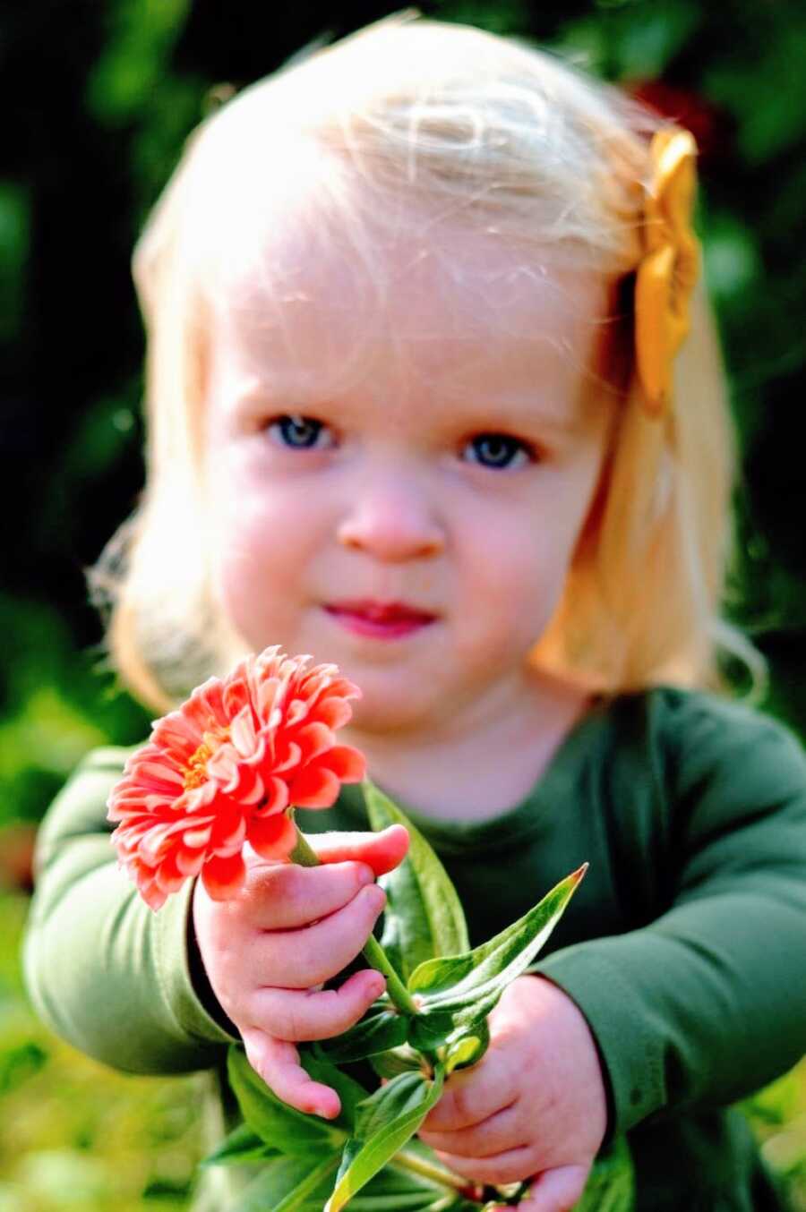 Little girl with dwarfism holds a flower during a photoshoot
