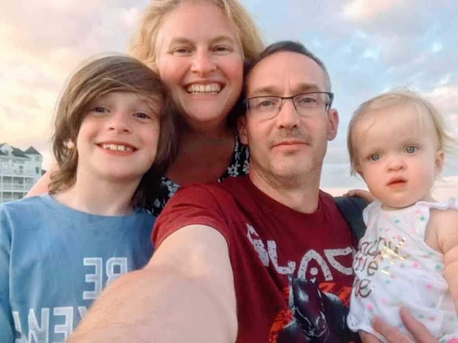 Family of four take a group selfie while watching the sun set on the beach