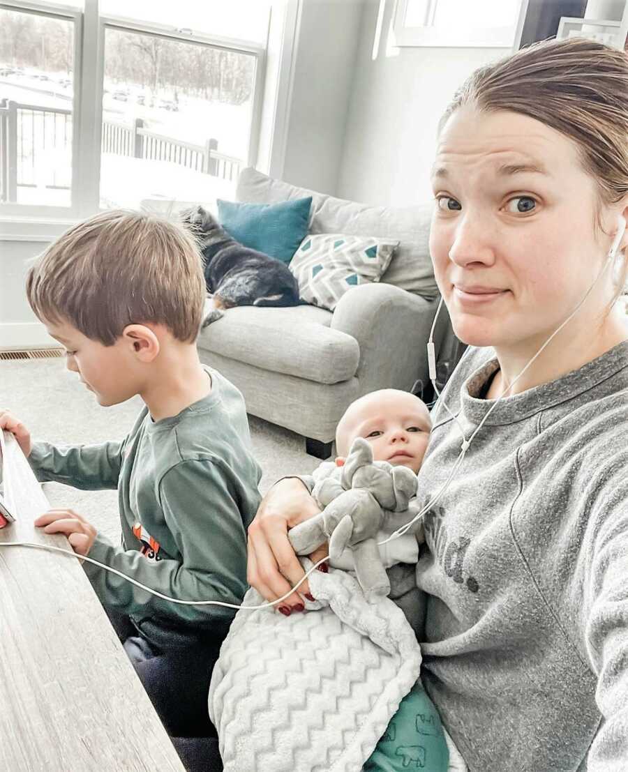 Mom holding baby in her arms while helping toddler with online homework