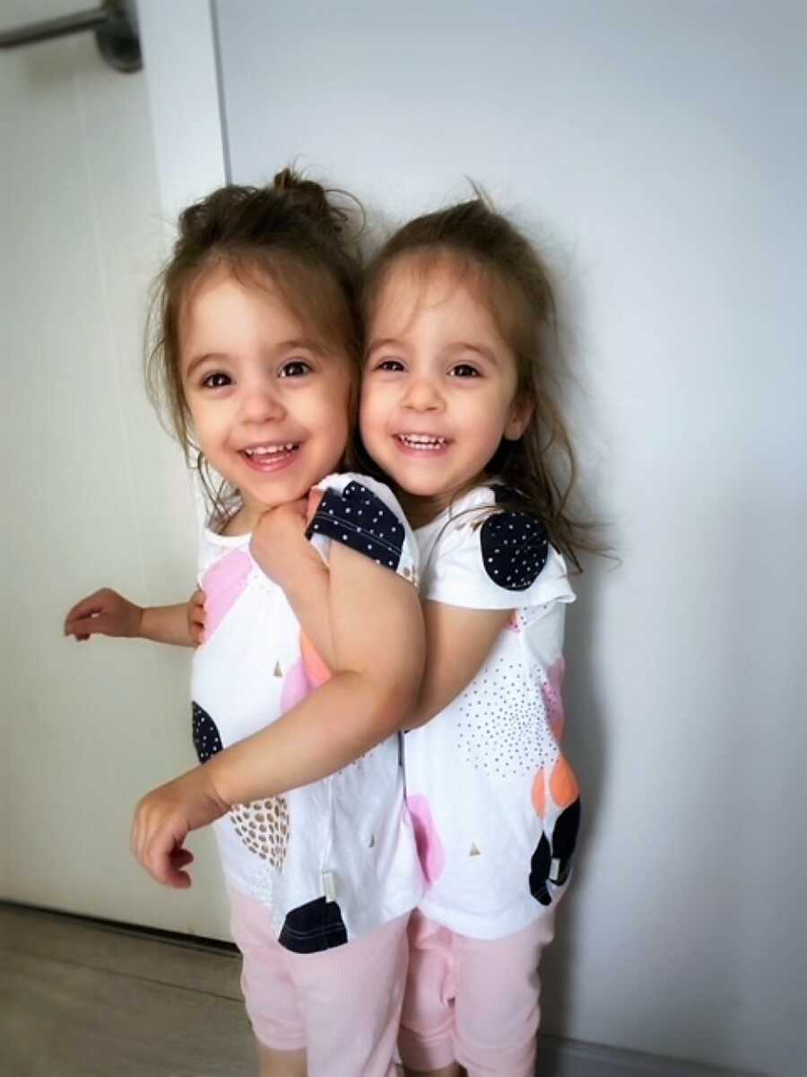 Identical twins sisters wearing matching outfits and hugging each other 