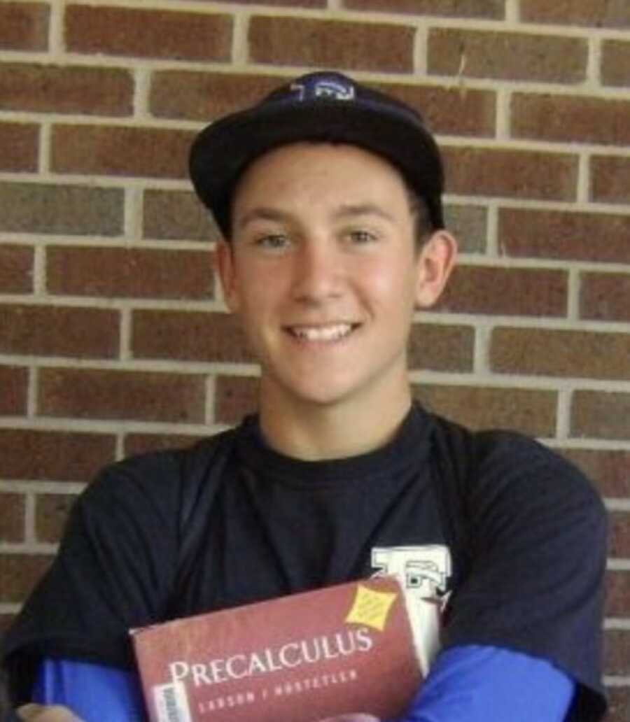 teen boy holding his books by a wall