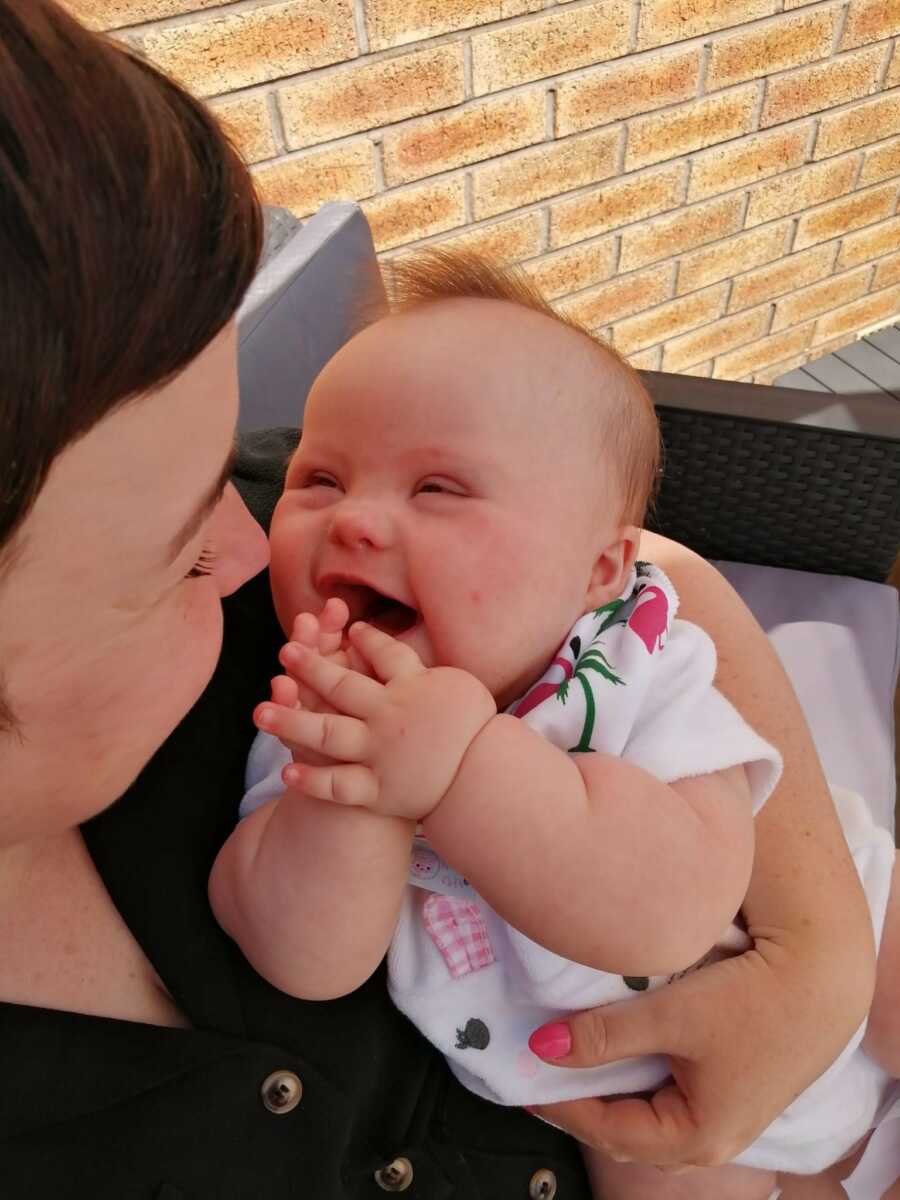 baby with down syndrome being held by her mom, smiling