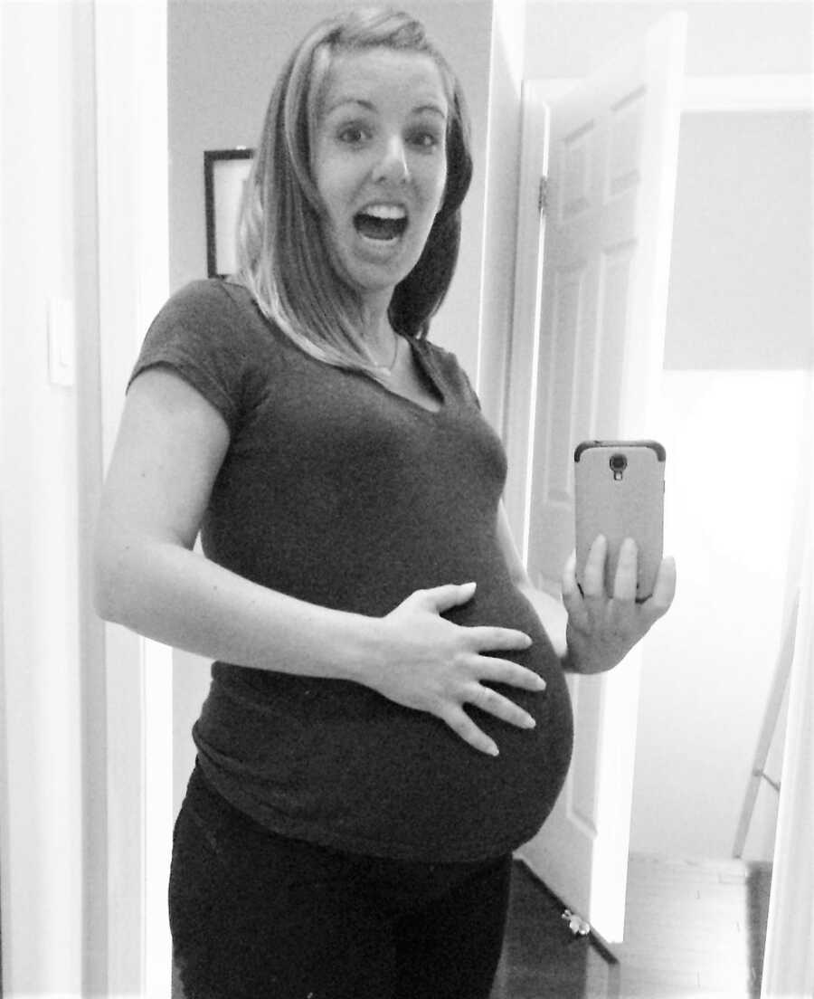 pregnant woman looks excited while taking mirror selfie holding belly 