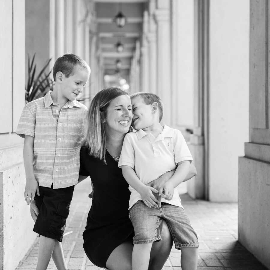 Mom diagnosed with OCD sitting down with her two boys smiling and hugging at a hall with large columns 