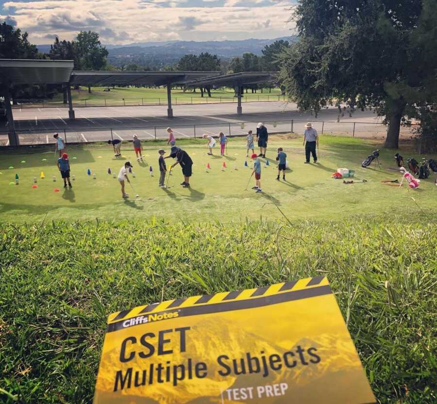 woman studying for her test while watching her kids play soccer