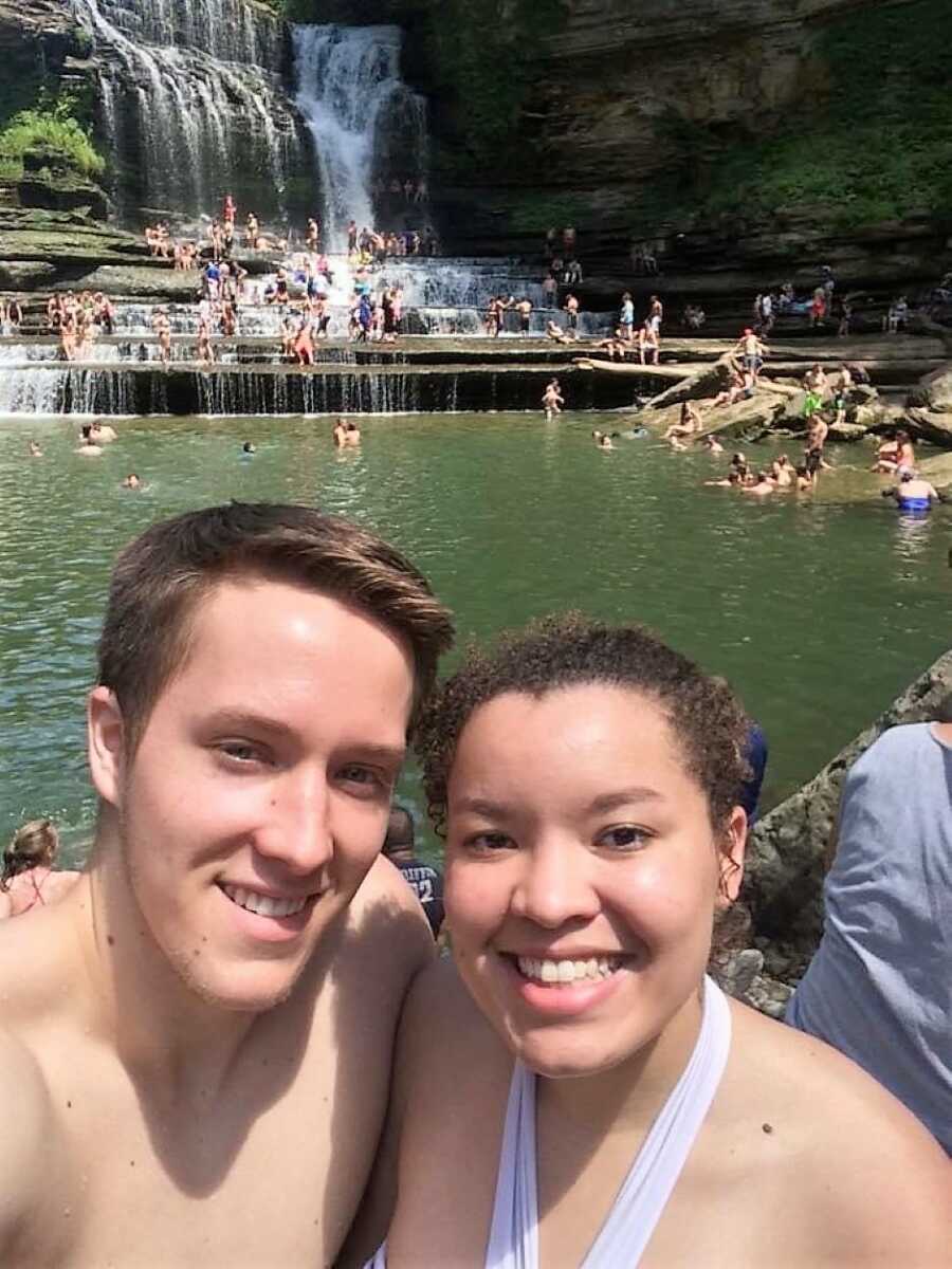 Highschool sweethearts in front of waterfalls smiling and hugging 