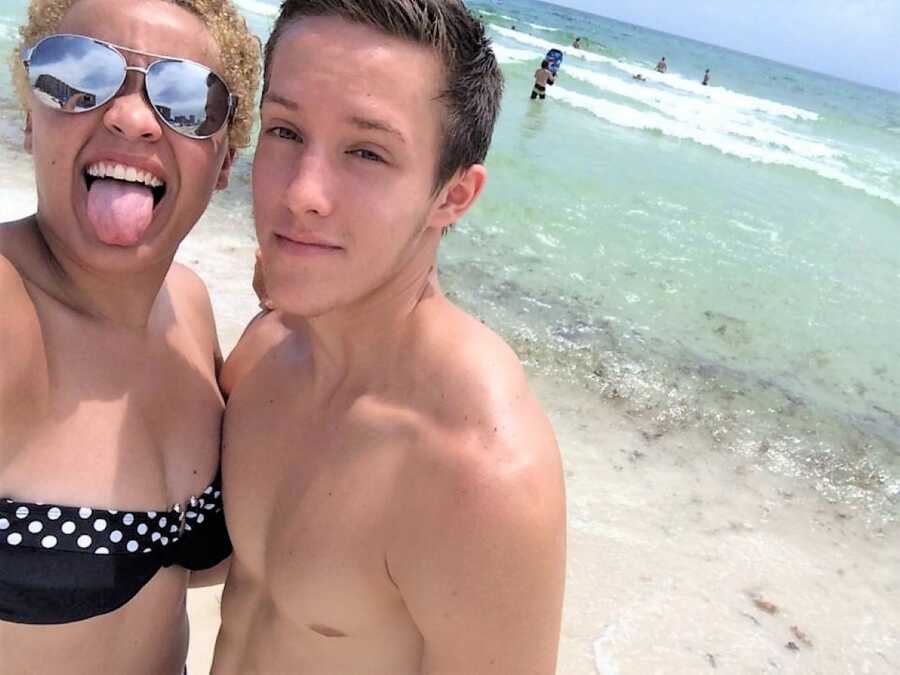 Highschool sweethearts at the beach smiling and sticking out tongue at camera 