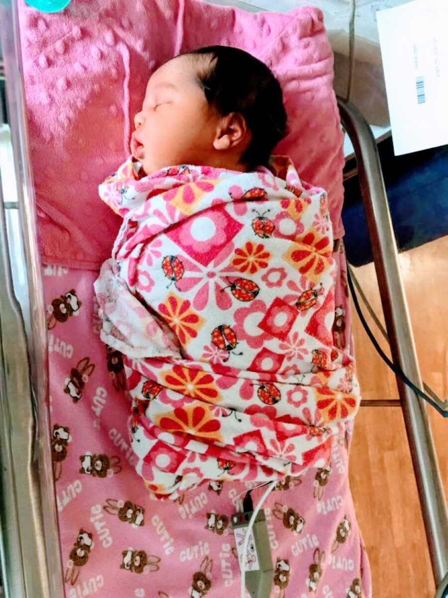 Newborn baby girl sleeps in the NICU while wrapping in a floral blanket