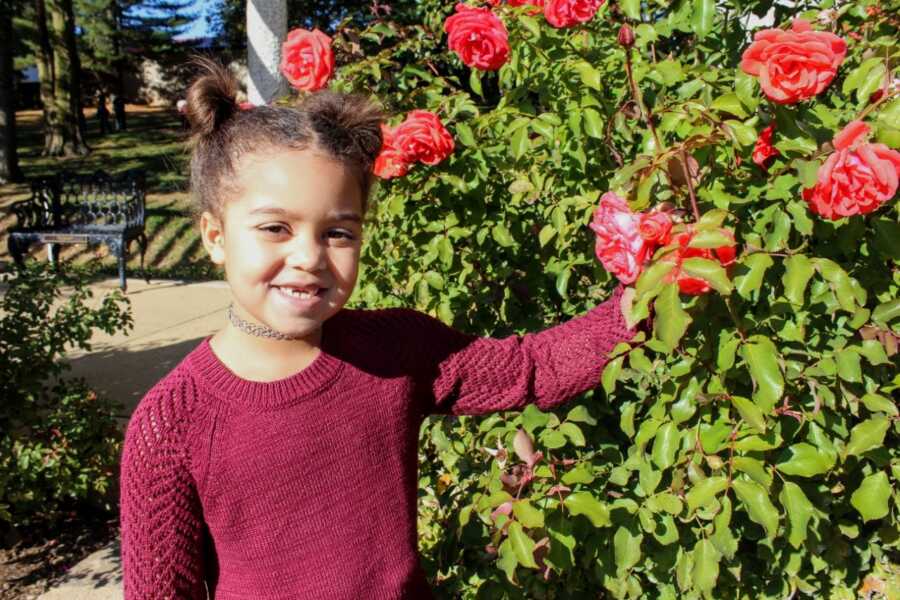 Medically complex child smiles for a photo next to a rose bush