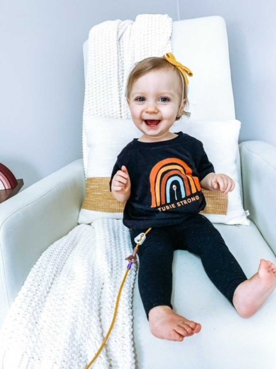 little girl sitting on the chair smiling with her feeding tube