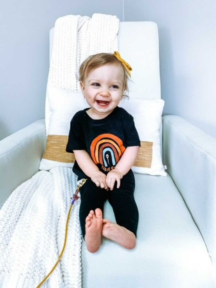 little girl sitting on the chair smiling with her feeding tube