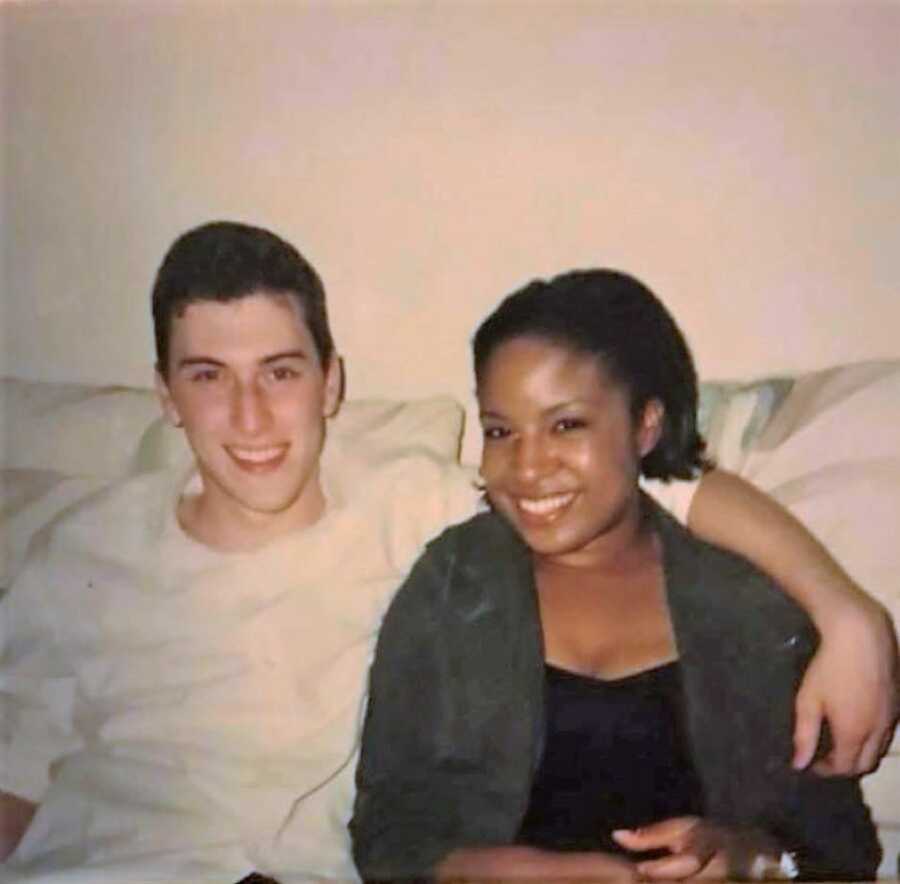 young interracial couple sitting in a couch, with boyfriend's arm resting on the girl's shoulders