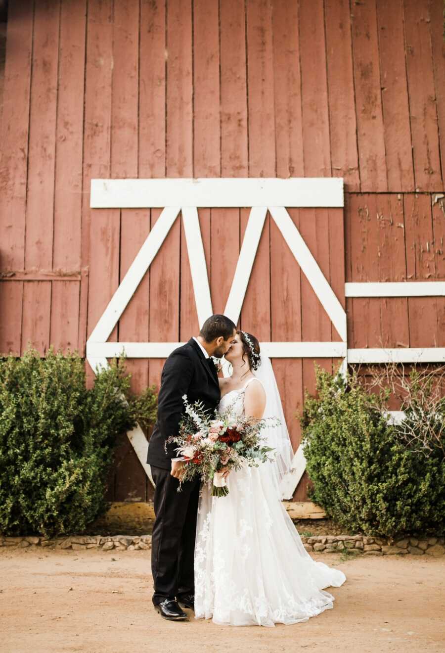 woman and husband kissing in front of barn