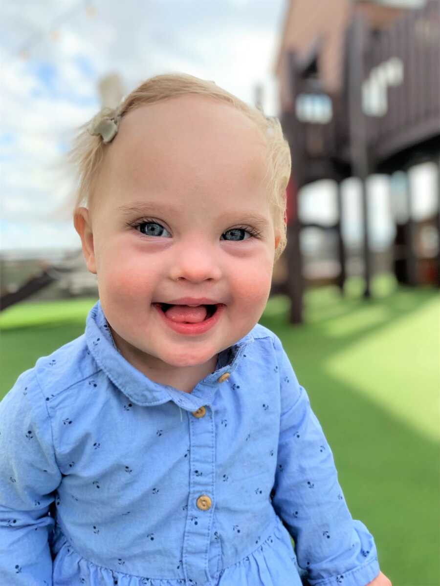 Baby girl with Down Syndrome looking at the camera and smiling big 