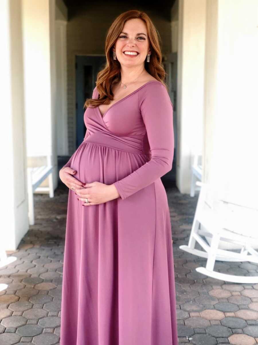 Woman pregnant with her first child smiles big in purple dress