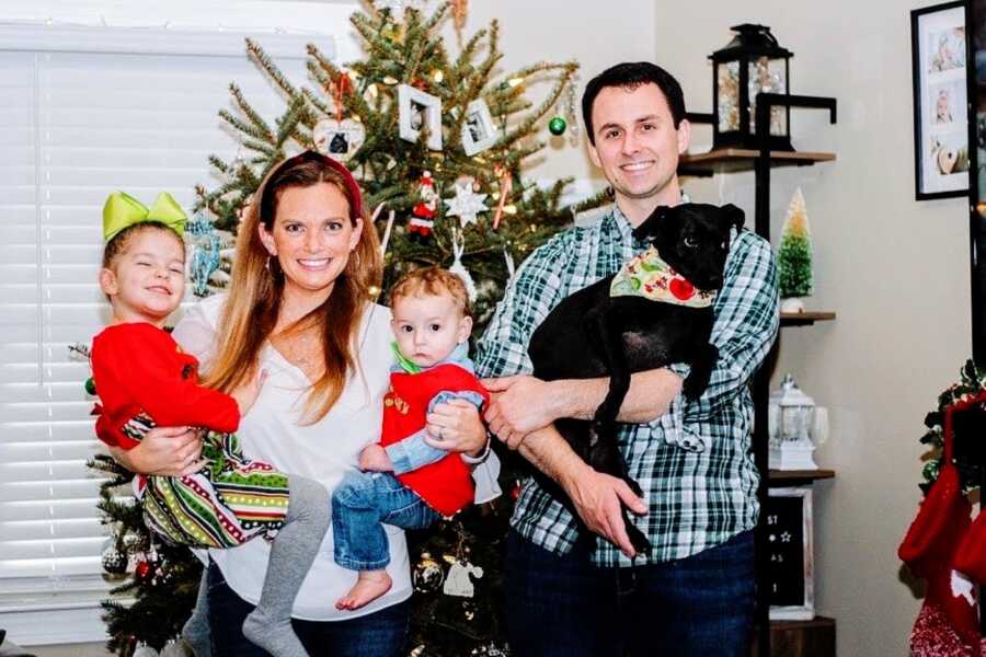 Family of four take Christmas photos together in front of their Christmas tree