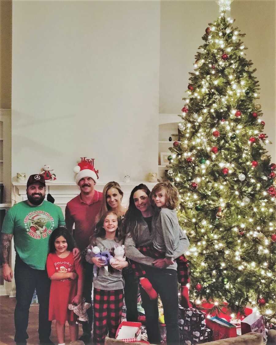 Lesbian mom and her blended family spending Christmas together next to a tall Christmas tree 