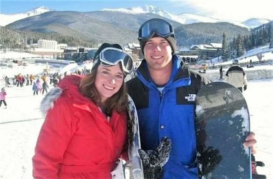 young couple who are skateboarding smile with mountains in the background