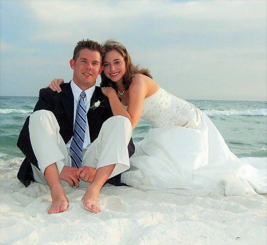 Couple during their wedding day sitting in the sand at the beach with the ocean in the background