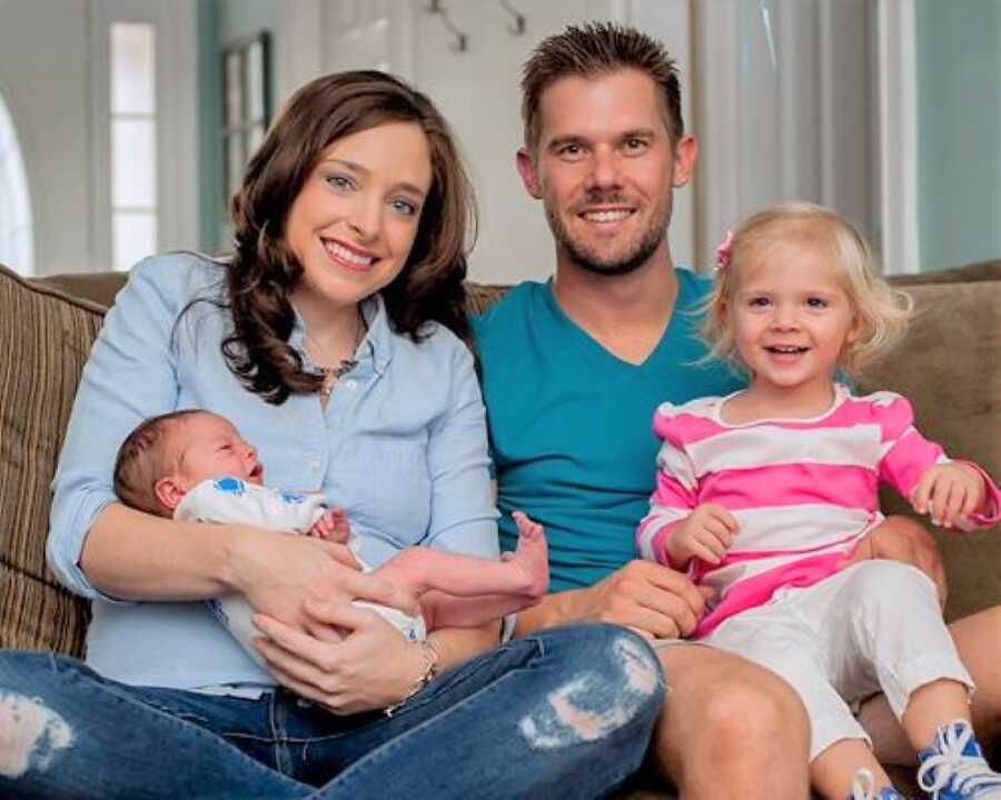 Mom and dad sitting in the couch with their newborn baby and toddle daughter