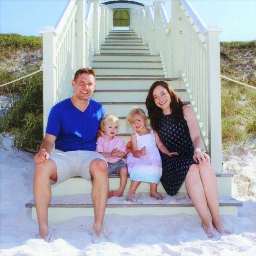 couple sitting at the bottom of white stairs with their two children at the beach