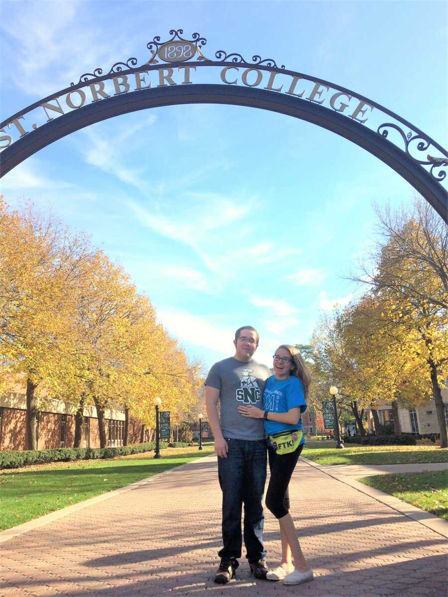 Woman living with rare chronic disease and her husband under the arch entrance of college