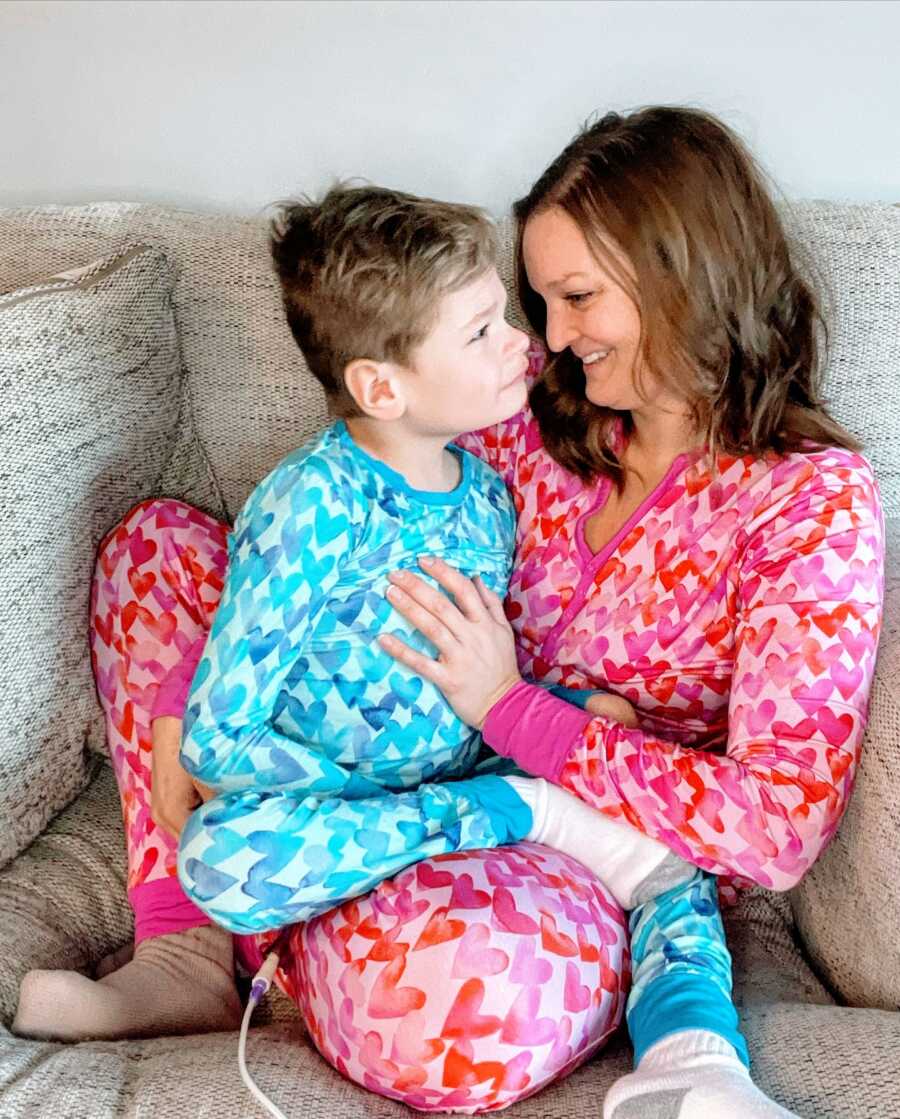 Mom and son cuddle on the couch in matching heart-patterned pajamas