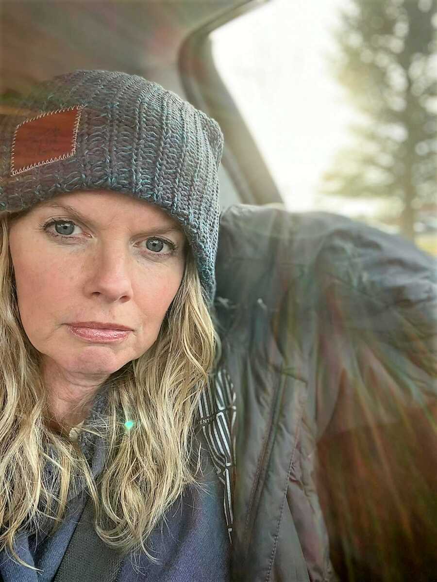 Woman sitting inside of a car with the sun shining through the window wearing winter clothing 