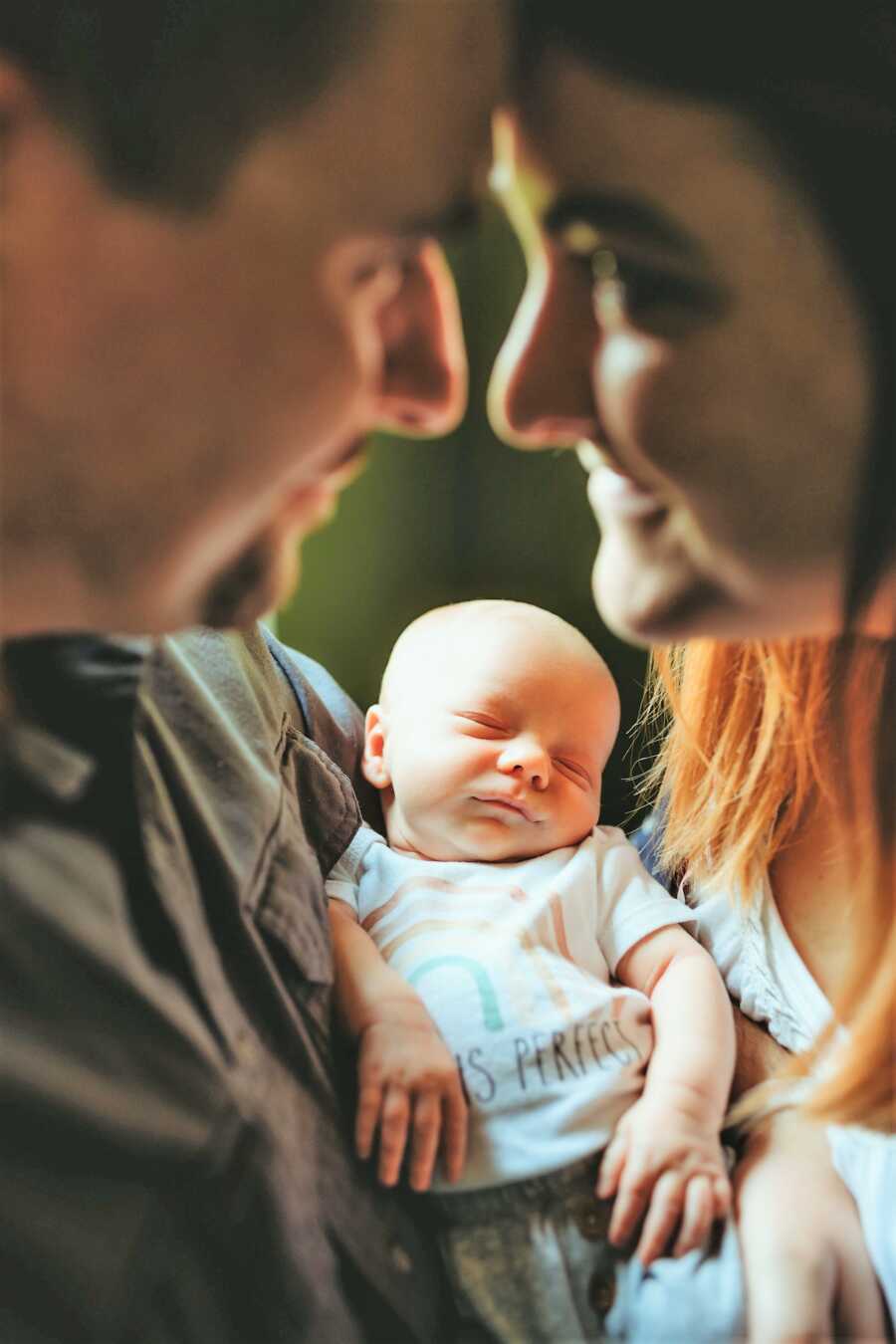 married couple staring at each other while holding newborn rainbow baby in their arms