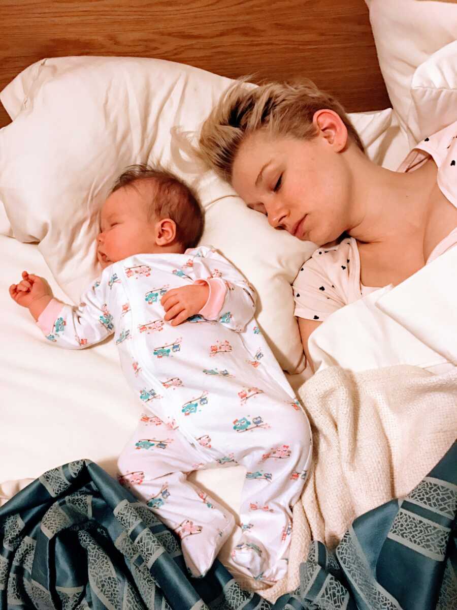 Mom looks worn out while she naps next to her newborn daughter in bed